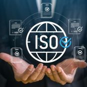 Photograph showing hands holding a digital graphic of a globe with "ISO" text and a blue checkmark, surrounded by five documents with checkmarks